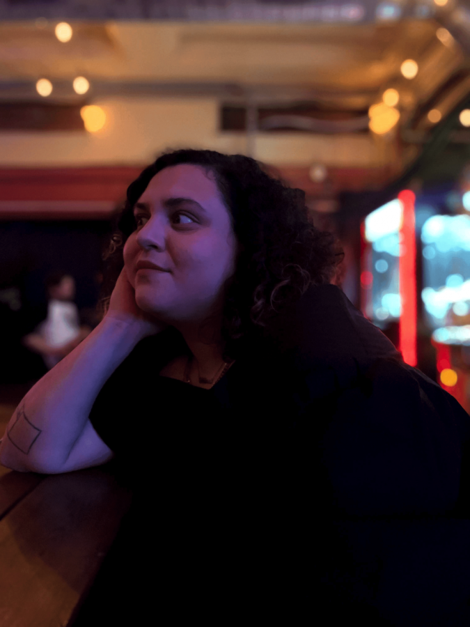 A photo of Cinthia Arias Auz seated in a low-lit room facing the left.